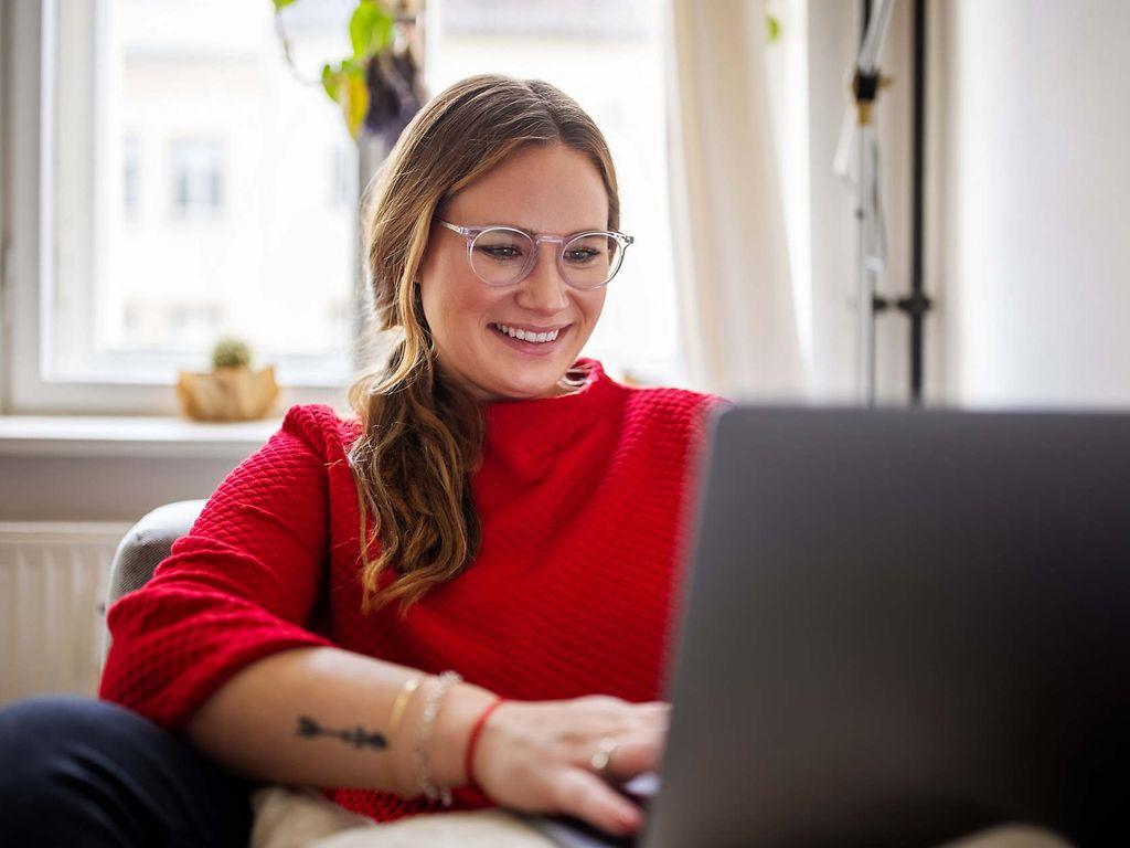 Bild: Junge Frau mit rotem Pullover schaut in Ihren Laptop.