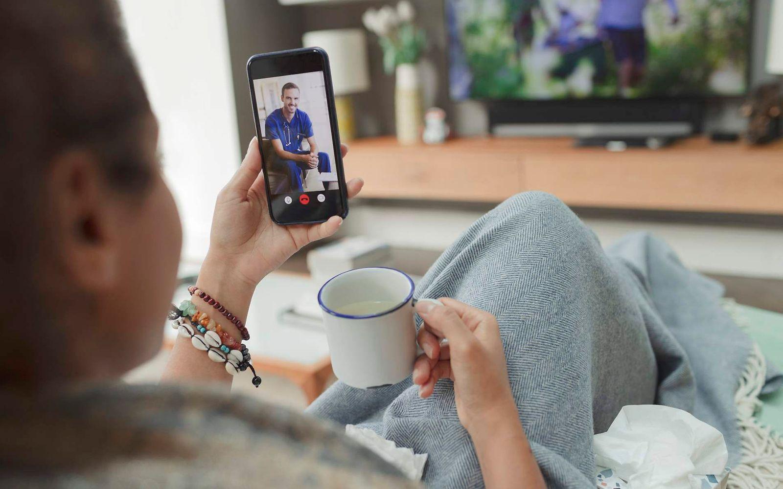 Bild: Frau sitzt auf dem Sofa zuhause und nutzt die Videosprechstunde.