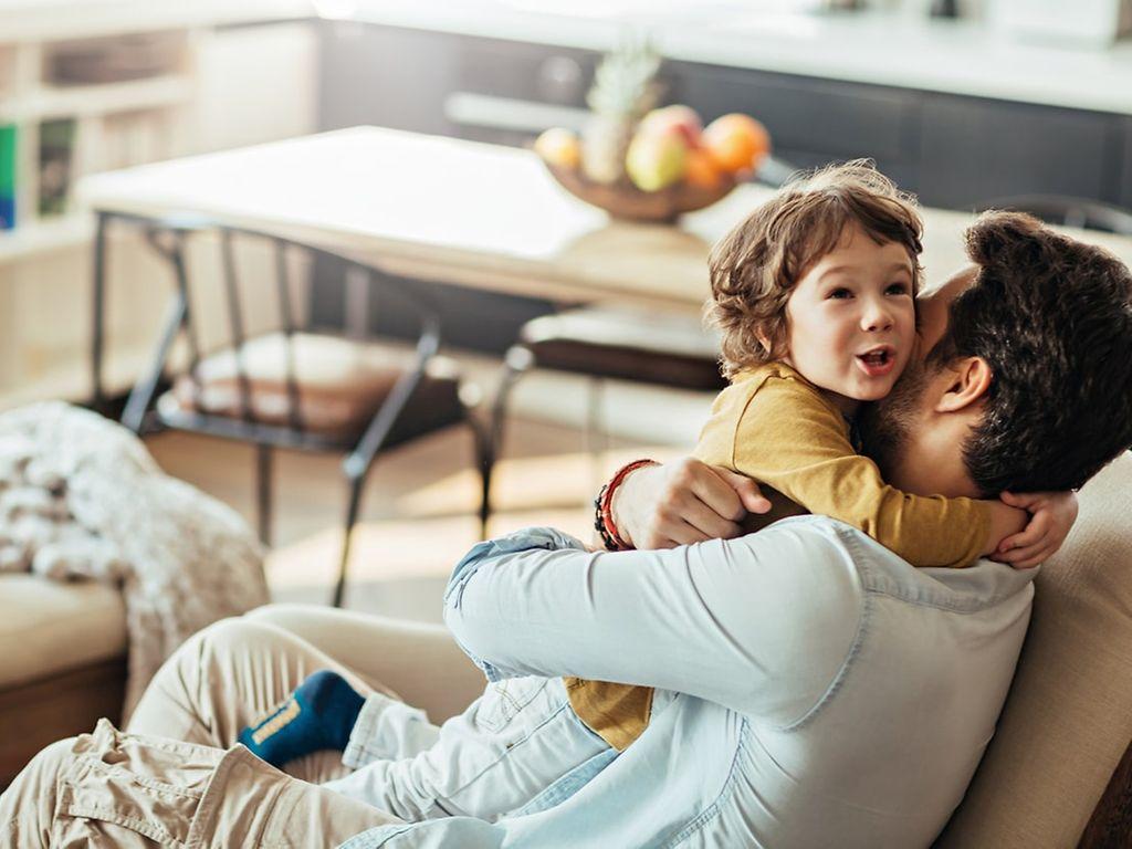 Bild: Vater umarmt sein Kind, eine fröhliche Situation im Familienalltag.