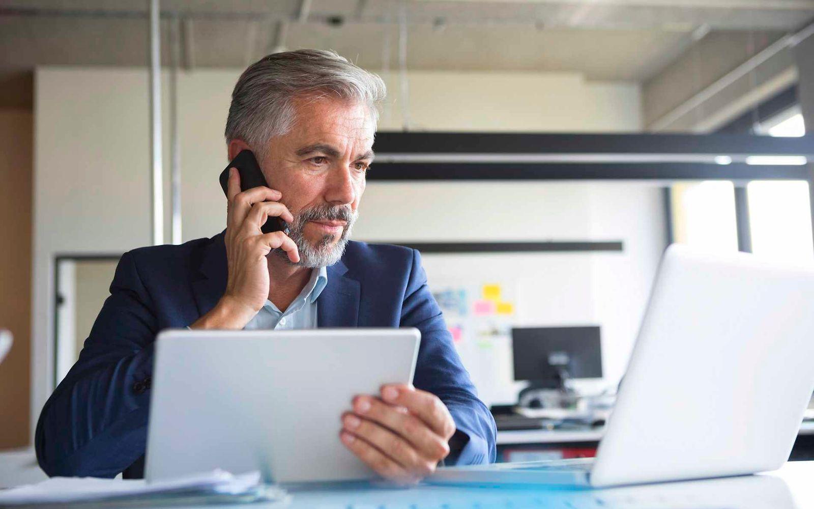 Bild: Älterer Business-Mann telefoniert und schaut auf einen Laptop.