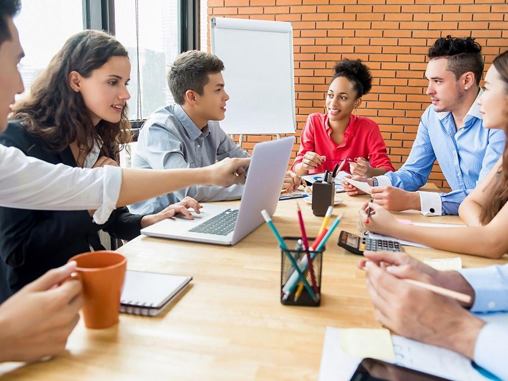 Junge Menschen sitzen am Tisch mit Laptop und diskutieren.