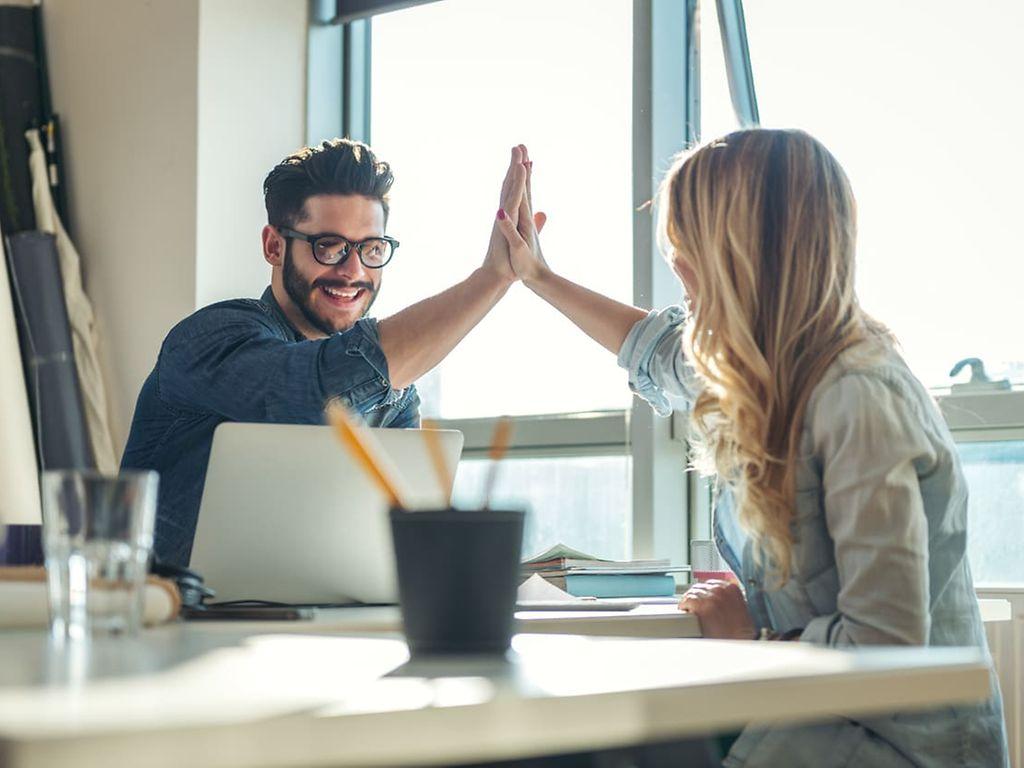 Bild: Frau und Mann geben sich ein High-Five am Schreibtisch.