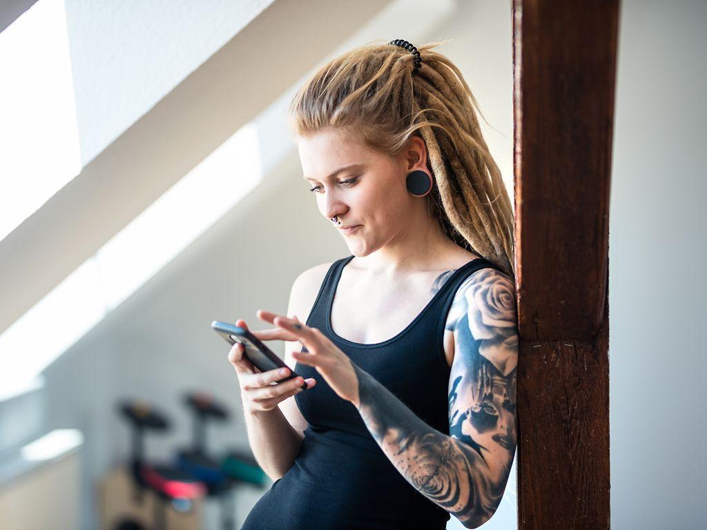 Bild: Frau mit Dreadlocks und Tattoo am Handy