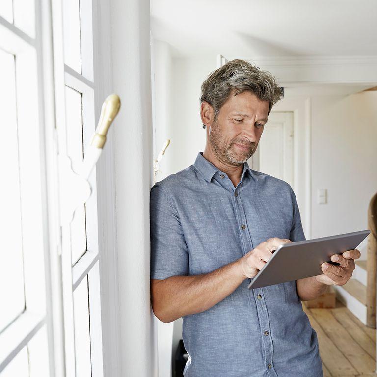 Mann steht mit Tablet am Fenster