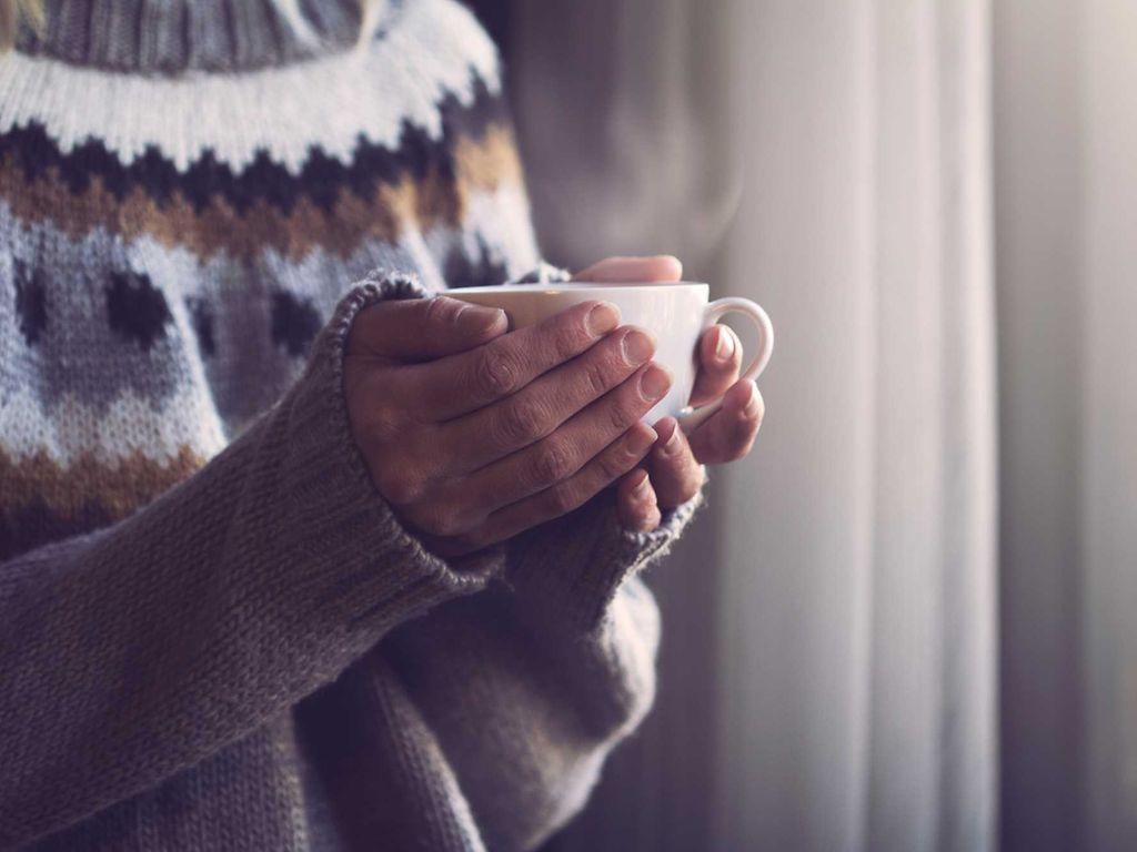 Grippe: Hände umschließen Tasse, aus der Dampf aussteigt.