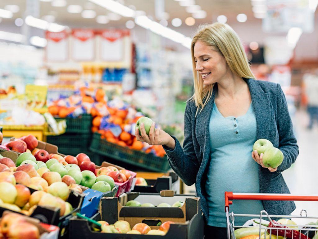 Eine Schwanger kauft Äpfel in der Obstabteilung eines Supermarkts