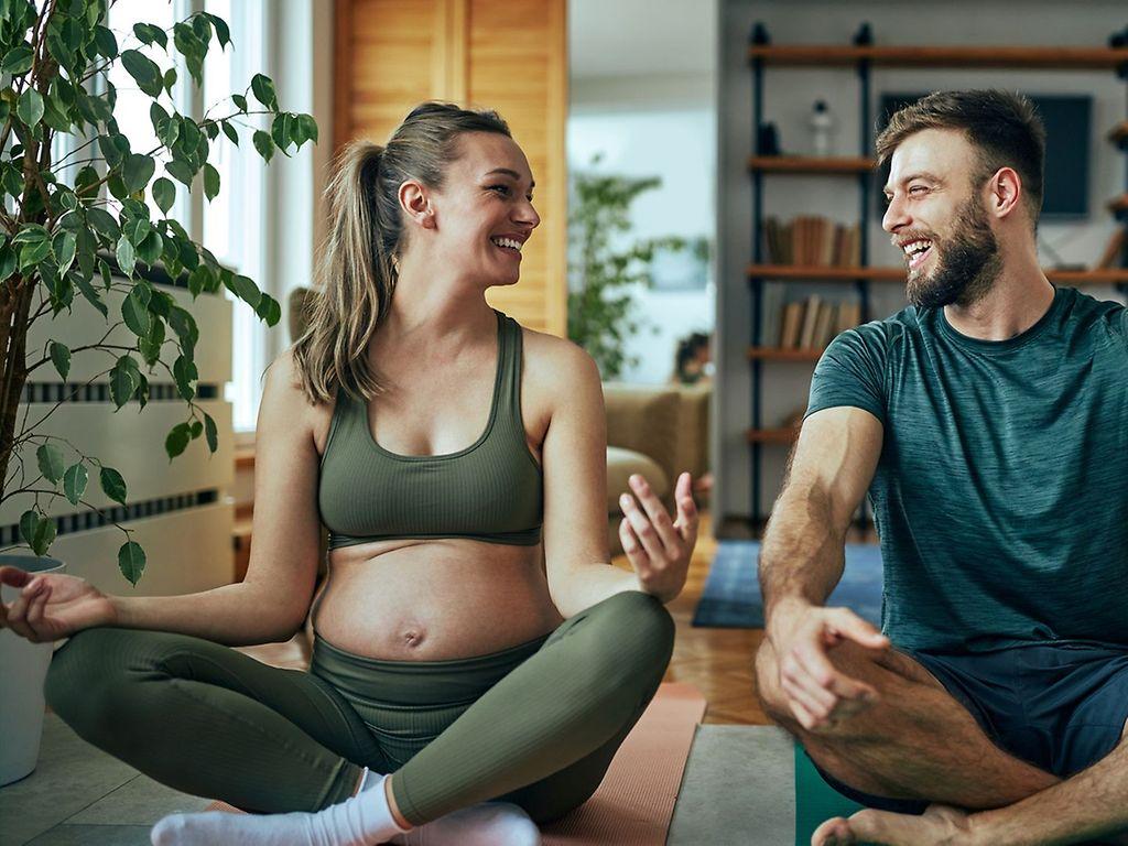 Symbolbild: Schwangere sitzt mit einem Mann auf dem Boden und entspannt.