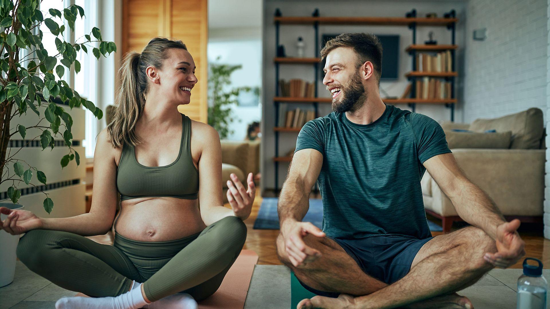Symbolbild: Schwangere sitzt mit einem Mann auf dem Boden und entspannt.