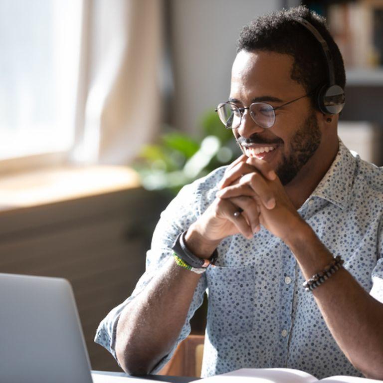 Onlineseminare: Ein Mann schaut auf seinen Laptop und freut sich.