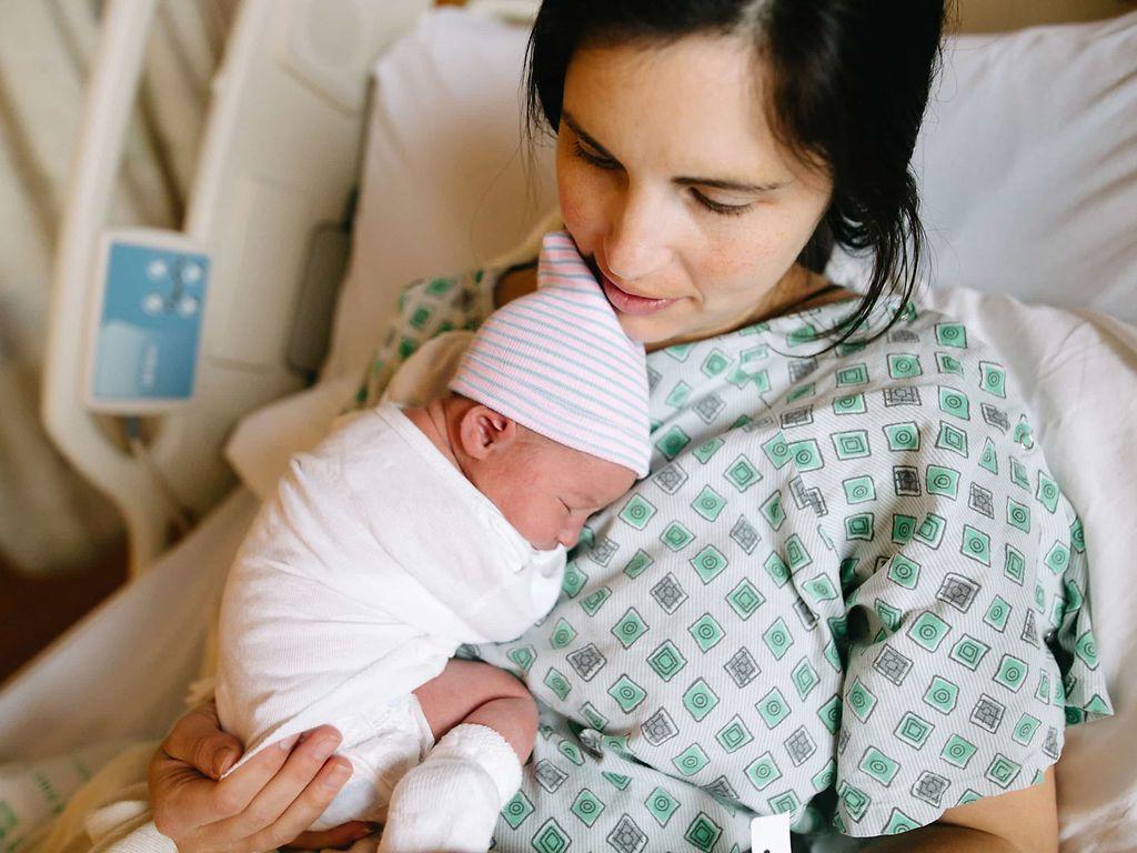 Ort der Geburt: Junge Frau liegt auf einem Krankenhausbett und hält ein Neugeborenes im Arm.