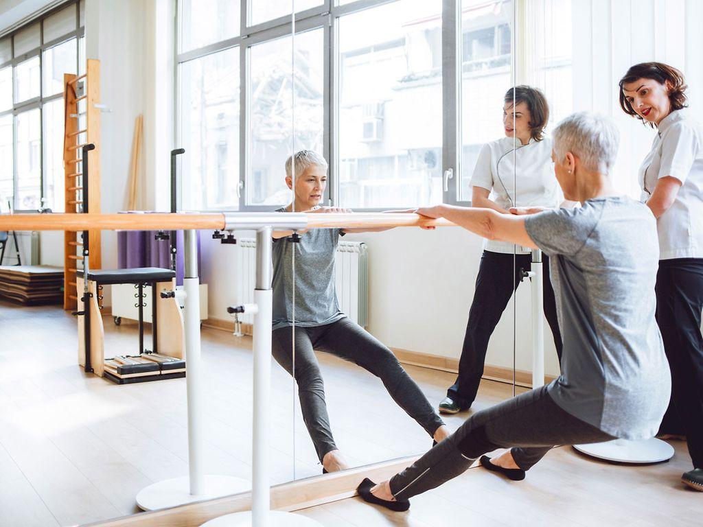 Rehasport: Frau und Trainerin an Stange am Spiegel.