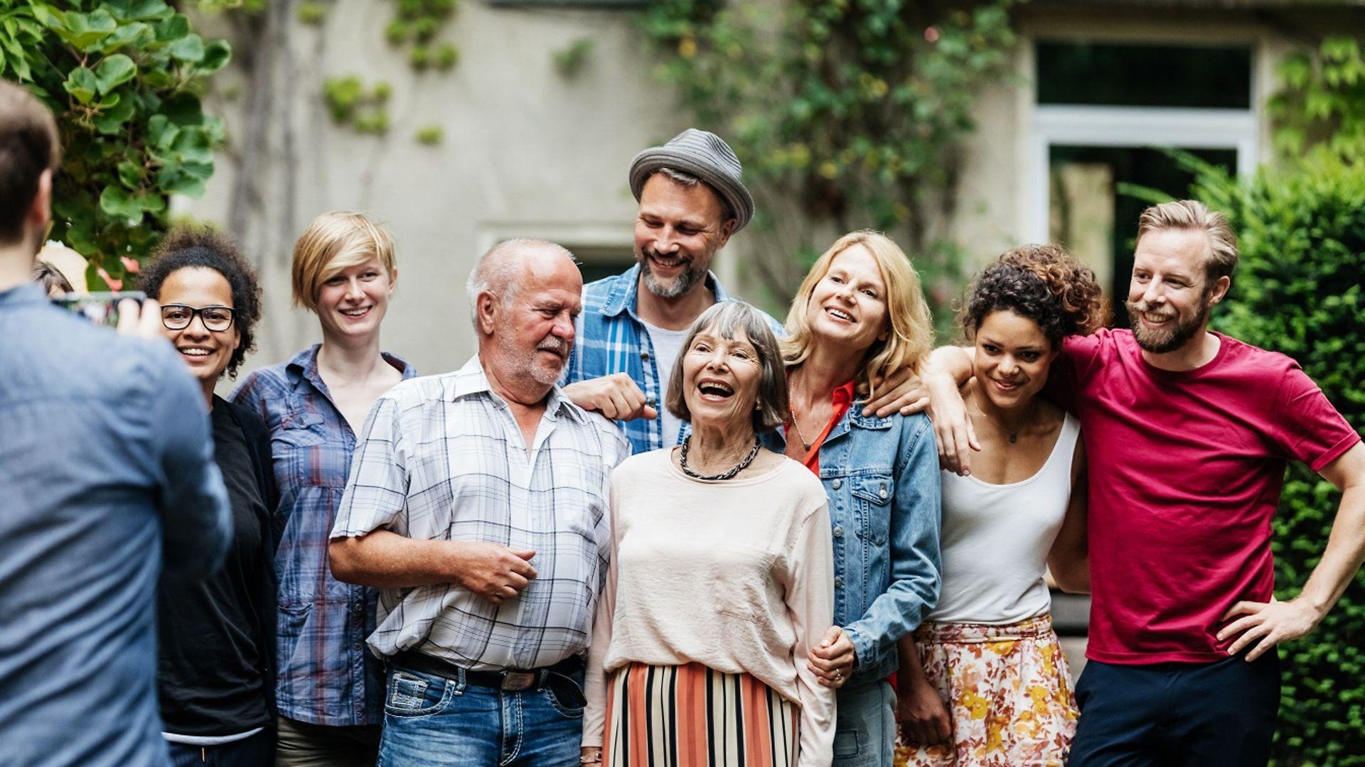 Bild: Ein Mann macht ein Foto von seinen Freunden und seiner Familie in einem grünen Hinterhof.